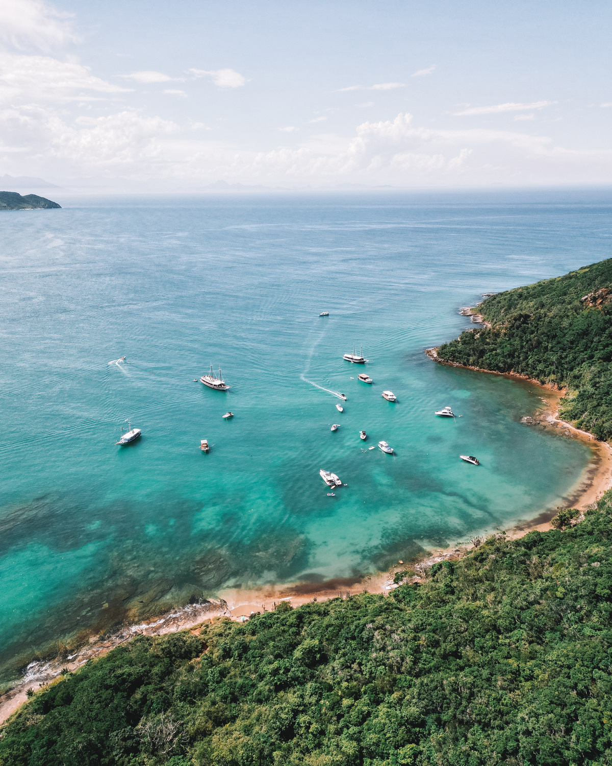 Panoramic view of a bay in Búzios with numerous anchored boats surrounded by lush greenery, highlighting boat tours as a top tourist activity.