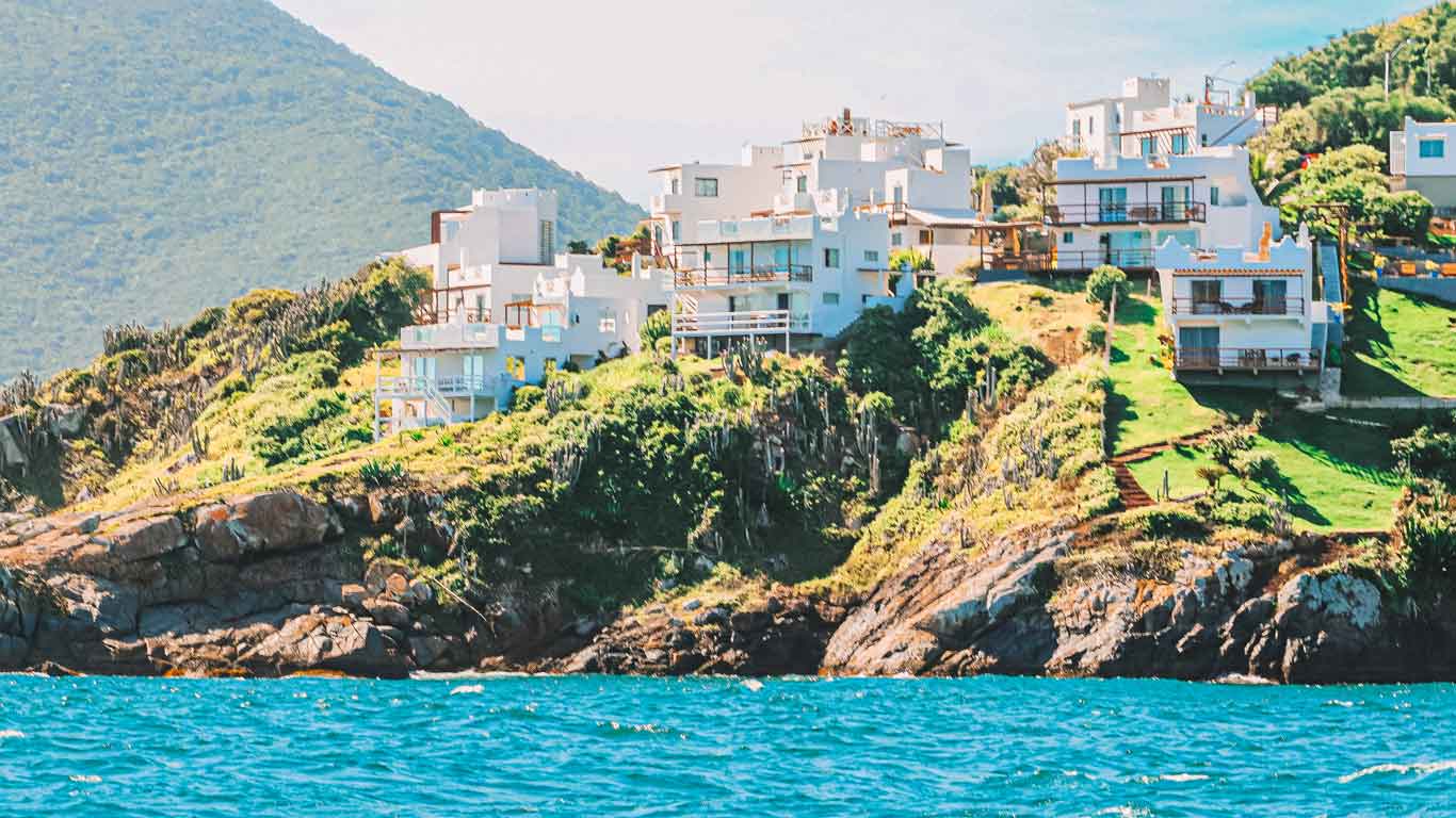 White houses nestled on a green hillside in Pontal do Atalaia, the prime region for renting vacation homes in Arraial do Cabo, shrouded in mist with the turquoise sea in the foreground.